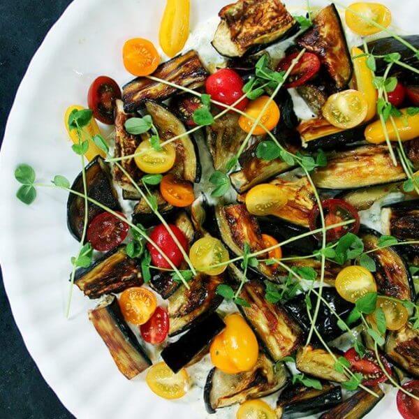 Roasted eggplant salad on a platter with tzatziki and tomatoes.