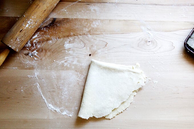 A floured board with a round of foolproof food processor pastry dough on it rolled out and folded into quarters. 