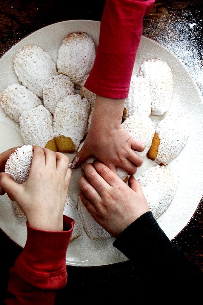 An overhead shot of hands reaching into grab madeleines on a platter.