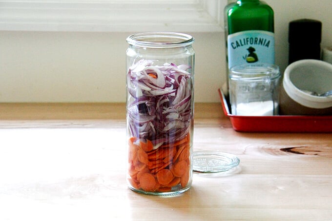 A jar filled with onions and carrots. 