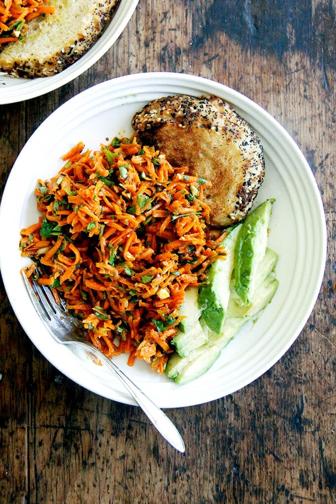 A bowl of Moroccan carrot salad aside bread and avocado.