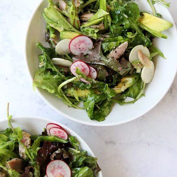 A bowl filled with a dinner salad: greens, tuna, radishes, avocado, shallot vinaigrette.