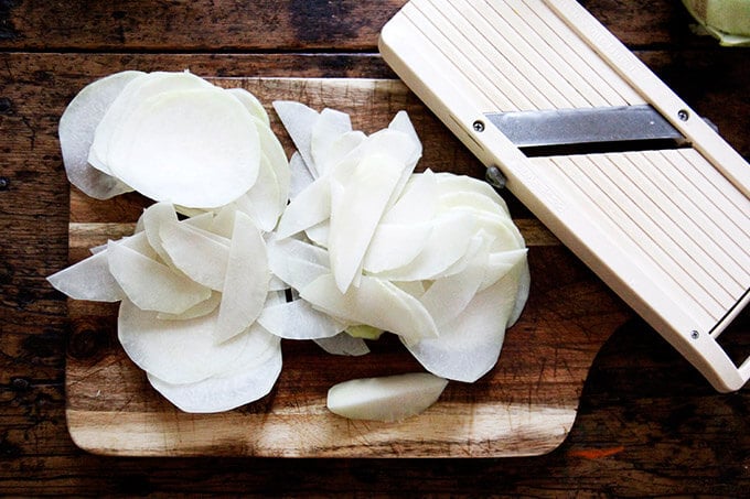 Thinly shaved kohlrabi on a board aside a mandoline. 