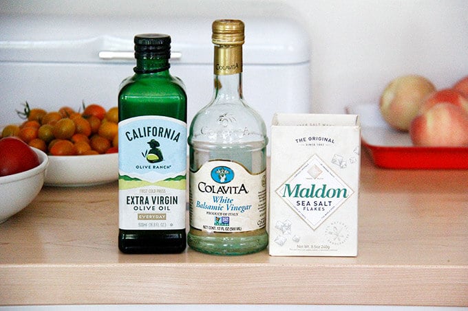 The dressing ingredients on a board: colavita white balsamic, california olive ranch olive oil, maldon sea salt.