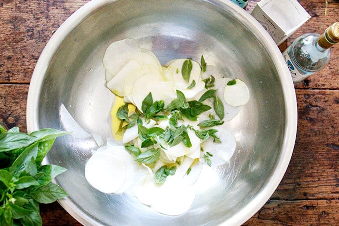 A large bowl of thinly shaved kohlrabi, salt, olive oil, vinegar, and herbs.