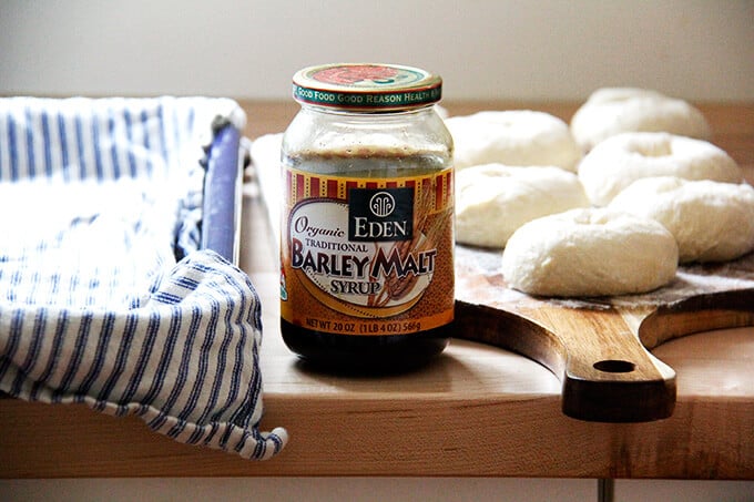 A jar of barley malt syrup aside resting, shaped bagels. 