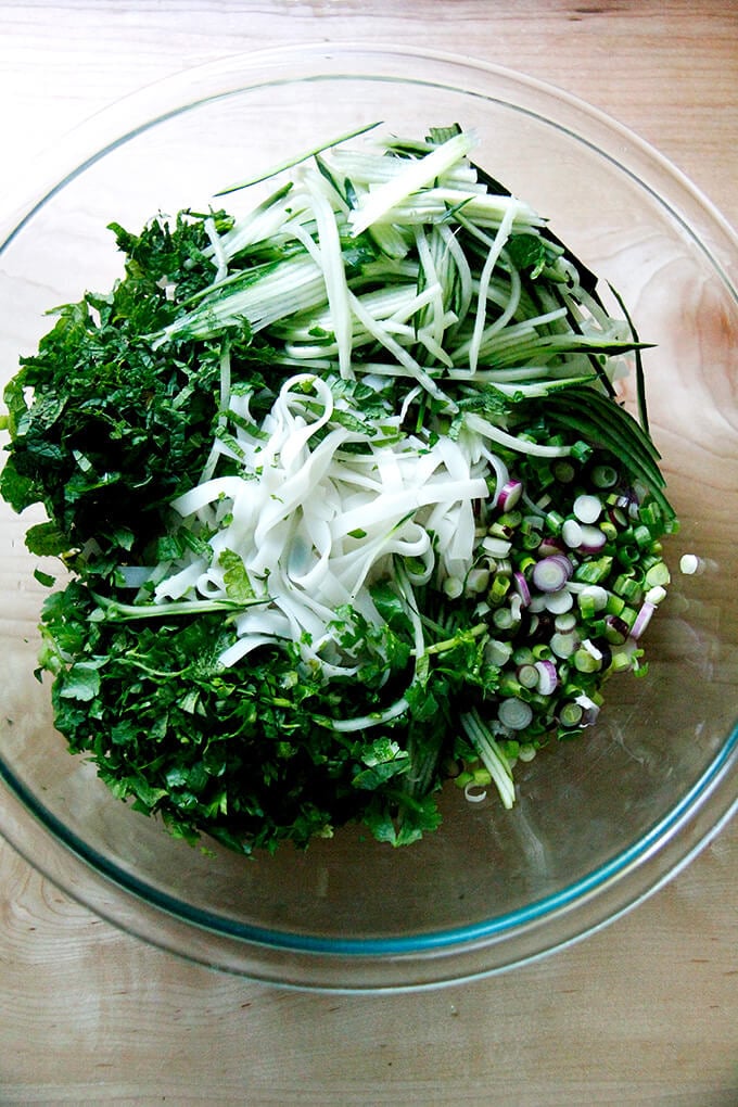 Cooked rice noodles with herbs and cucumbers in a bowl. 