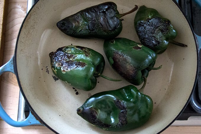 Blistered poblano peppers in a skillet.