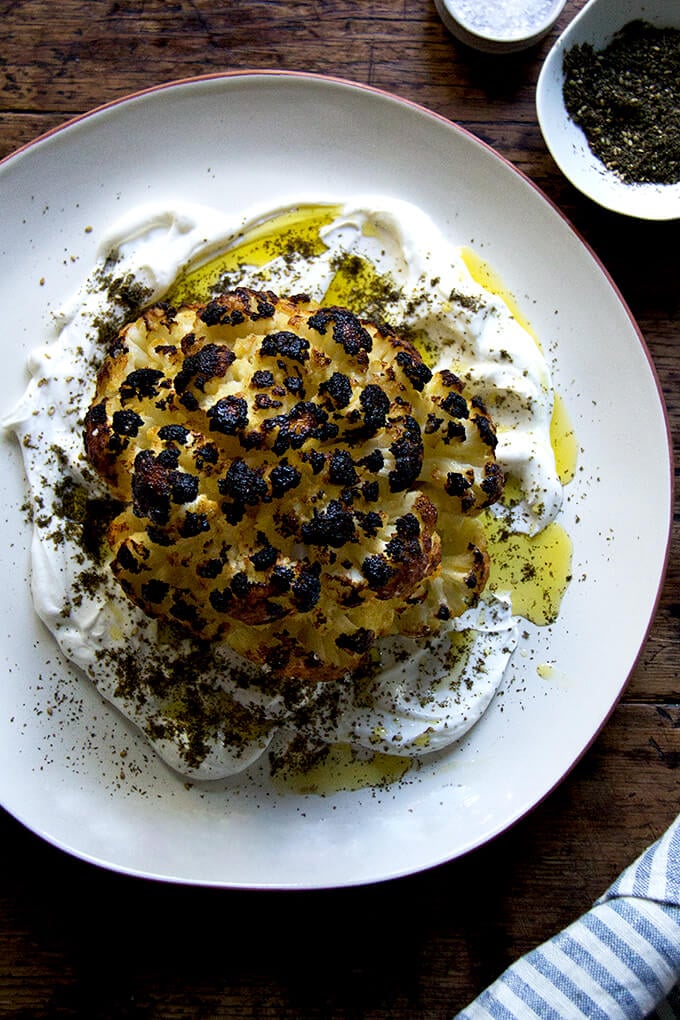 A an overhead shot of a plate of whole roasted cauliflower with lemony yogurt sauce.