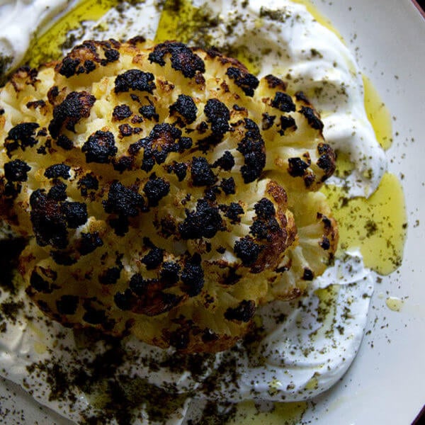 A an overhead shot of a plate of whole roasted cauliflower with lemony yogurt sauce.