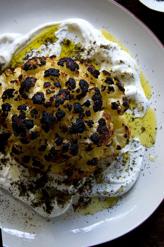 A an overhead shot of a plate of whole roasted cauliflower with lemony yogurt sauce.