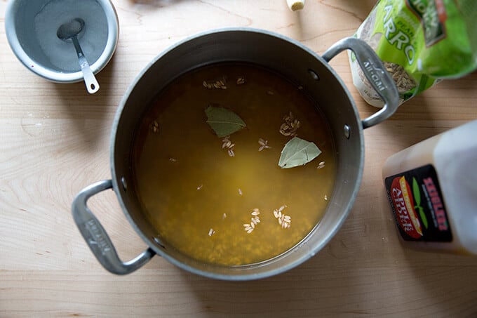 A pot filled with farro, water, apple cider, salt, and bay leaves.