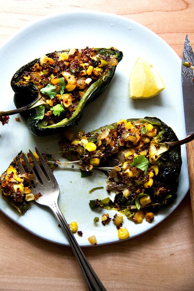 A pan of blistered poblano peppers stuffed with quinoa, corn, and Monterey Jack on a plate. 