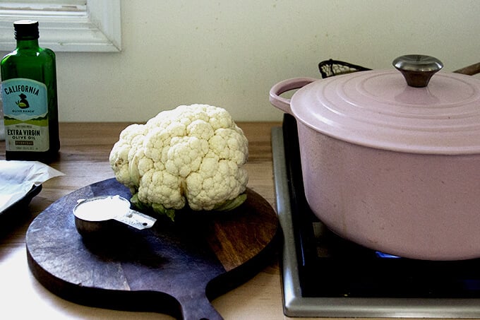 A head of cauliflower on a board aside a measuring cup filled with salt.