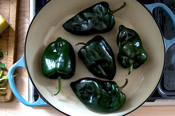 Poblanos being blistered in a skillet on the stovetop. 