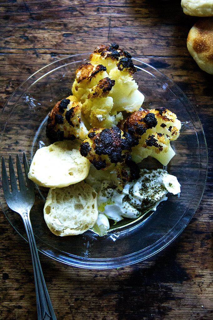 A plate with florets from a whole roasted head of cauliflower, lemony yogurt sauce, and bread.
