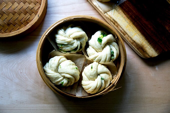 A steamer basket fitted with 4 scallion buns ready to be steamed.