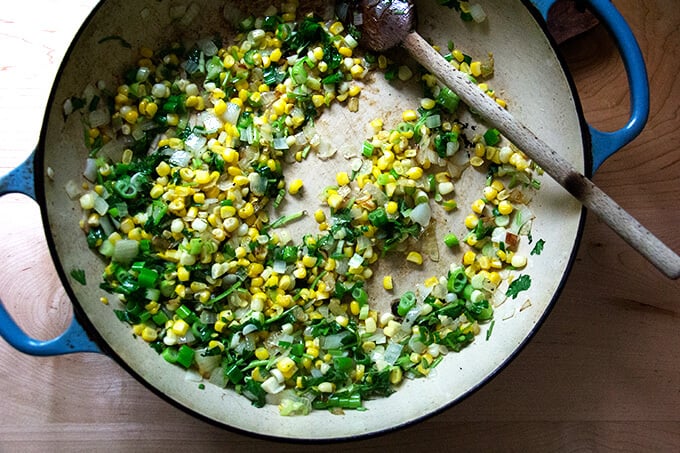 Sautéed vegetables in a skilet: onion, corn, scallions, and herbs. 