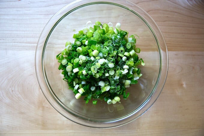 A bowl of sliced scallions, seasoned with oil and salt.