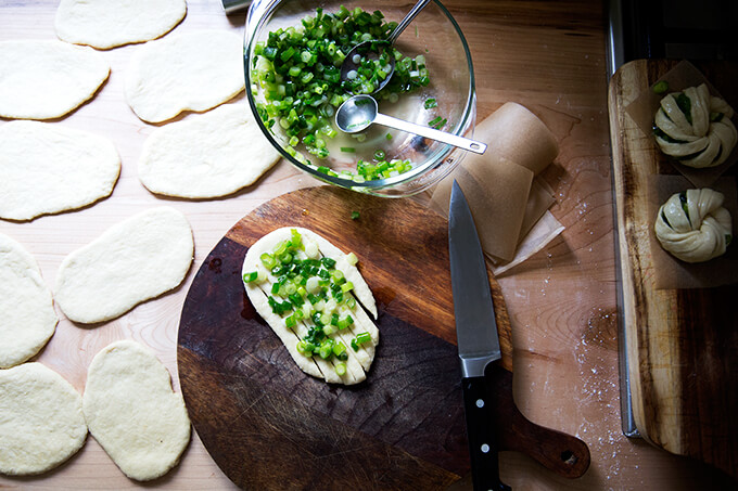 A board with a round of dough topped with scallions.