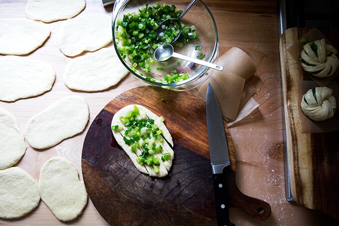 A board with a round of dough topped with scallions.