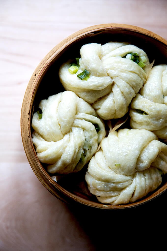 Overhead shot of a steamer basket open to reveal 4 steamed scallion buns. 