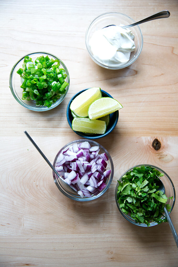 A countertop with all of the black bean soup garnishes: sour cream, scallions, lime, red onion, and cilantro.