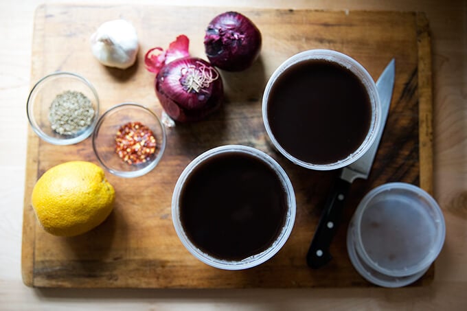 A board with ingredients for black bean soup: orange, cumin, chili flakes, garlic, onion, beans.