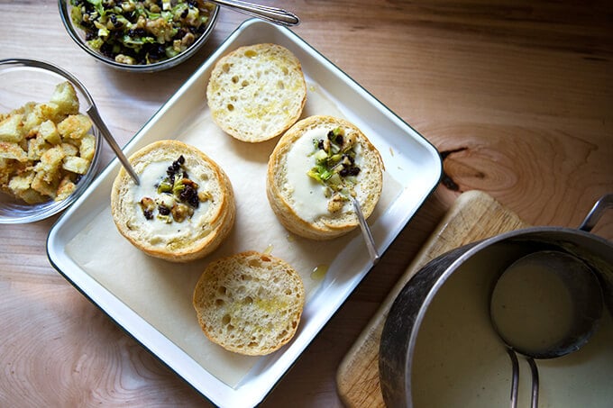 An overhead shot of two bread bowls filled with cream of celery soup with walnut salsa on a tray.