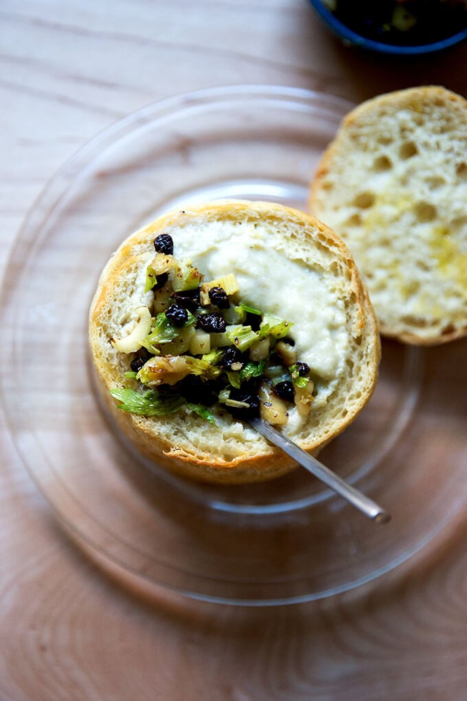 An overhead shot of a bread bowl filled with cream of celery soup with walnut salsa.