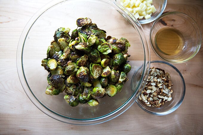 A bowl of roasted Brussels sprouts aside bowls of Manchego, almonds, and reduced balsamic. 