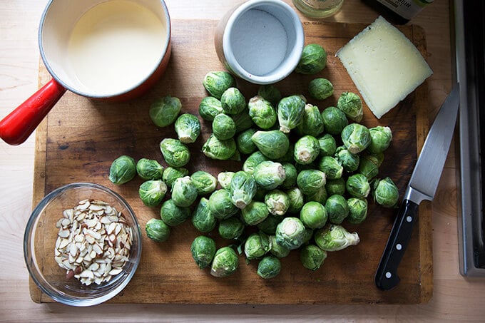 A cutting board with Brussels sprouts, almonds, salt, manchego, and vinegar.