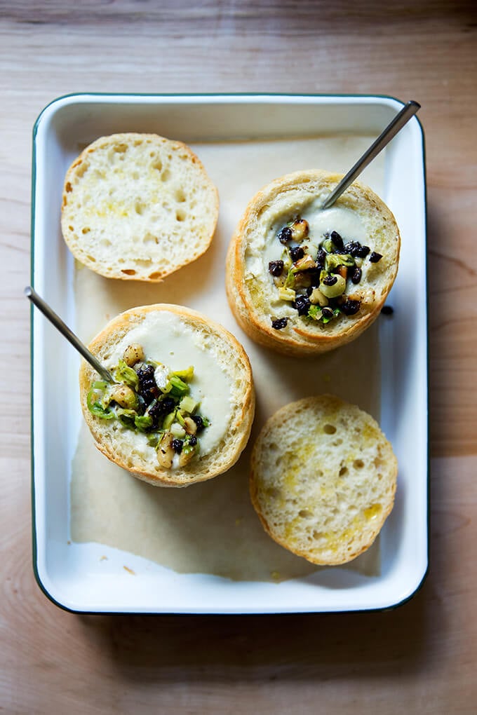 An overhead shot of two bread bowls filled with cream of celery soup with walnut salsa.