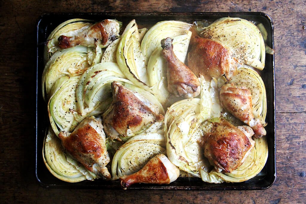 A sheet pan of partially roasted chicken legs and cabbage.