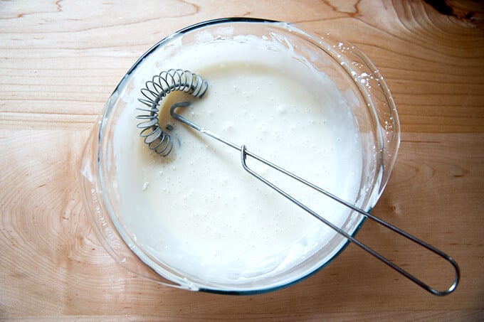 A large bowl filled with the maple glaze all whisked up with a whisk inside. 