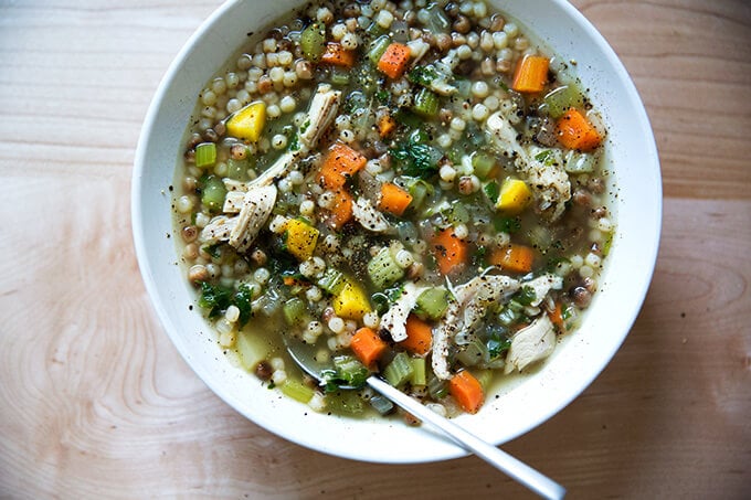 A bowl filled with homemade chicken soup with fregola and a spoon. 