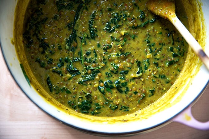 A pot of curried lentils with kale simmering stovetop in a Dutch oven.