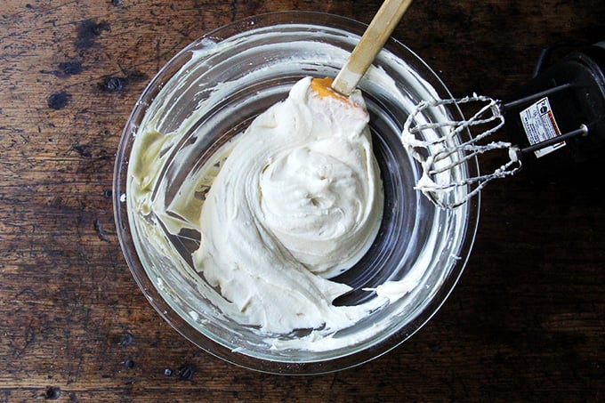 cream cheese frosting in a large bowl with handheld mixer next to bowl. 