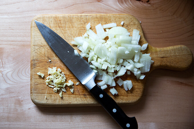 minced garlic and diced onions on a cutting board with a knife