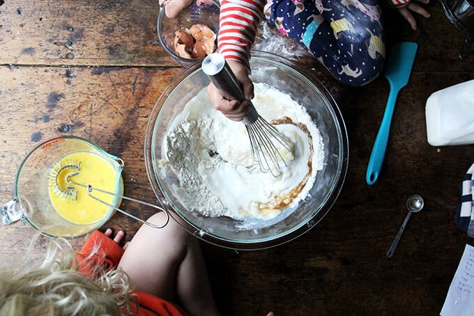 Two children mixing a one-bowl buttermilk birthday cake sitting on top of a table. 