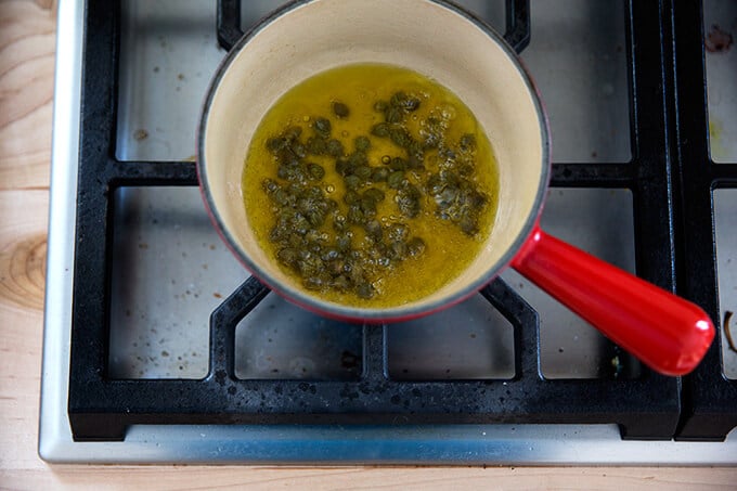 olive oil heating with capers in a small saucepan stovetop