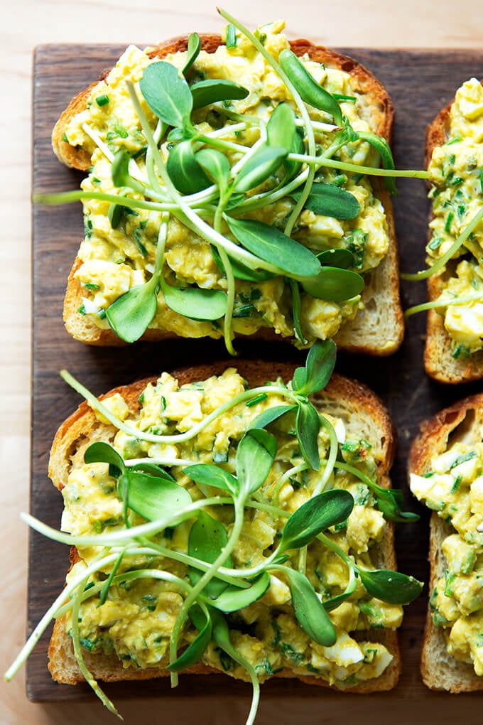 Slices of toasted sourdough bread topped with avocado-egg salad and sprouts.