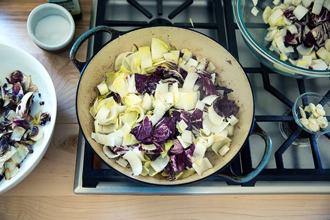 A sauté pan with olive oil, garlic, endive and radicchio.