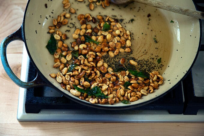 A braiser pan with ghee, mustard seed, curry leaves, and peanuts.