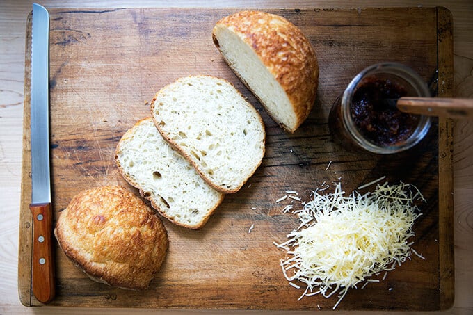 Sliced peasant bread, a jar of apple chutney, and grated cheese on a board.