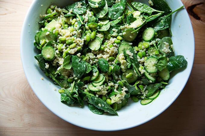 A bowl of baby spinach, edamame, sliced cucumber, brown rice, and avocado tossed with miso dressing.