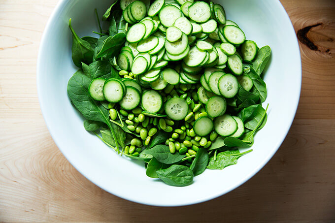 A bowl of baby spinach, edamame, and sliced cucumber.