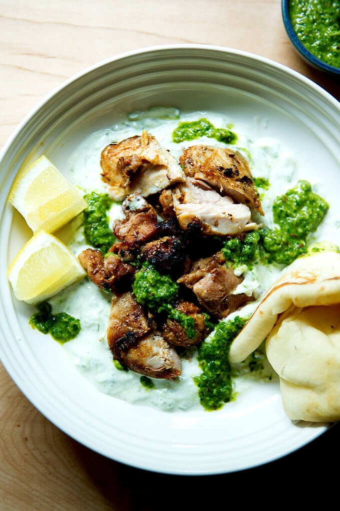 A platter of grilled, smoky chicken, cucumber-yogurt sauce, skhug, pita, and lemon