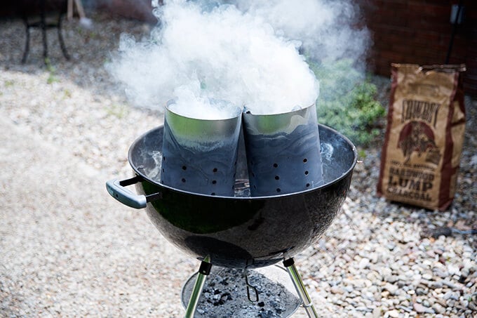 A weber grill filled with two smoking chimney starters.