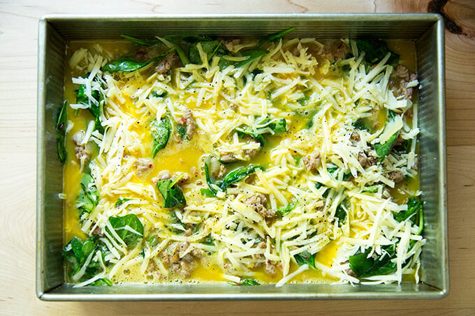 A 9x13-inch pan filled with eggs, cheese, sausage, spinach, and onions.